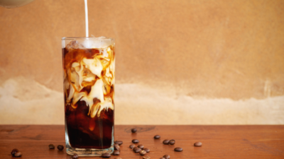 Cold brew coffee with ice and a splash of cream, served in a tall glass with coffee beans scattered around.