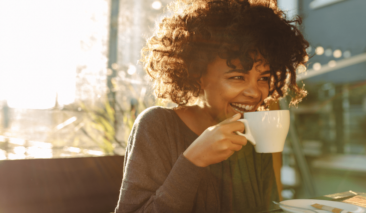 A cheerful young woman drinking coffee at a cafe, feeling refreshed and energized.