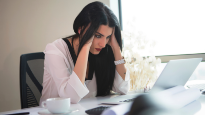 A stressed businesswoman at her desk struggling with work pressure, ready to take a break with a cup of Beneve Calm Brew for stress relief.