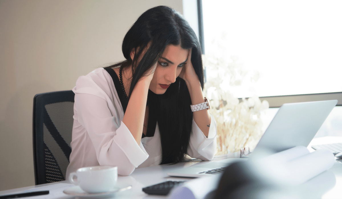 A stressed businesswoman at her desk struggling with work pressure, ready to take a break with a cup of Beneve Calm Brew for stress relief.