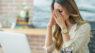 A stressed woman sitting at her desk with her hands on her face, experiencing workplace burnout and exhaustion.